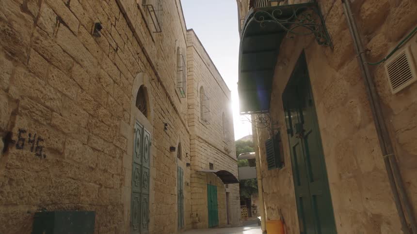 Bright sun flare beams down a narrow stone alleyway in an ancient, historic city