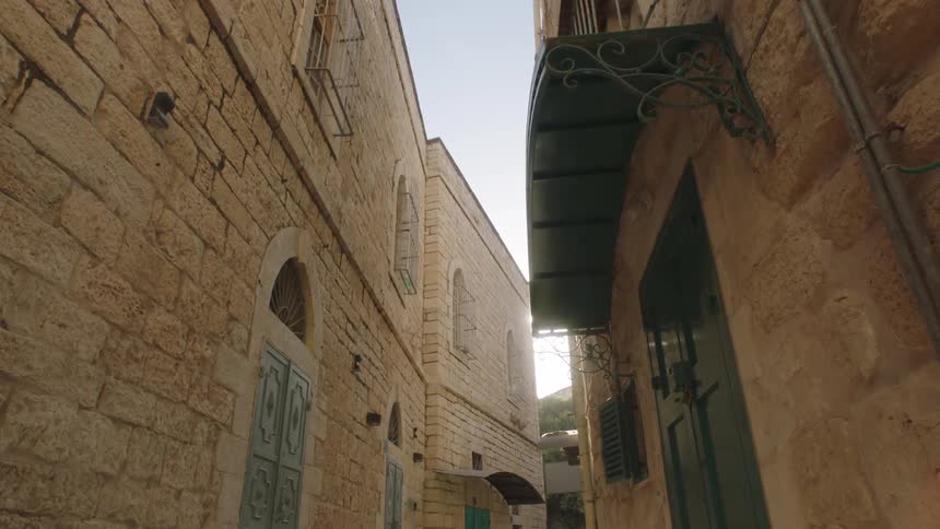 A slow dolly shot reveals the bright sun flaring between ancient stone buildings in a narrow alleyway