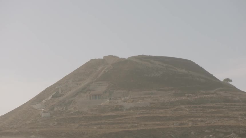 A slow tilt down reveals the majestic Herodium, King Herod's palace-fortress, in the hazy Judean desert