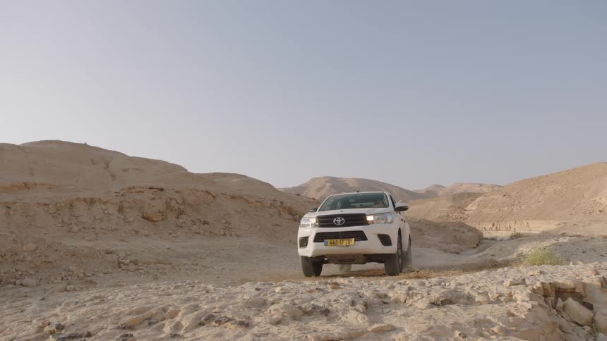 A white off-road truck drives slowly towards the camera on a rugged, rocky desert trail in slow motion