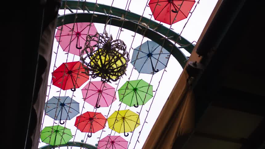 A slow zoom-out from a low-angle view of a whimsical art installation featuring colorful umbrellas hanging from an arched ceiling