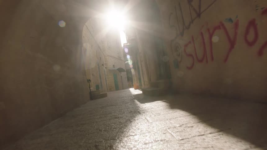 Low angle reverse tracking shot moves through a stone tunnel alleyway with graffiti towards a bright sun flare