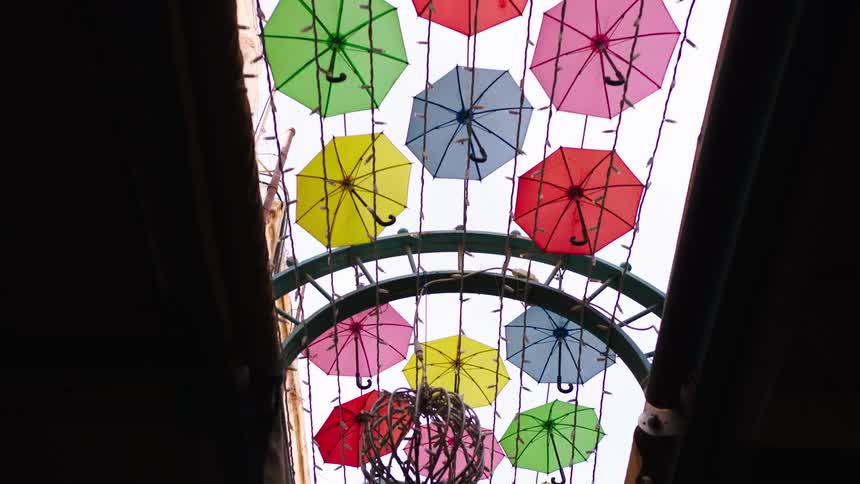 Looking up at a beautiful and colorful art installation of many small umbrellas hanging over an alleyway