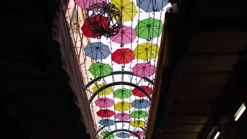 Colorful umbrellas hang from the ceiling as a beautiful art installation in a narrow, covered street