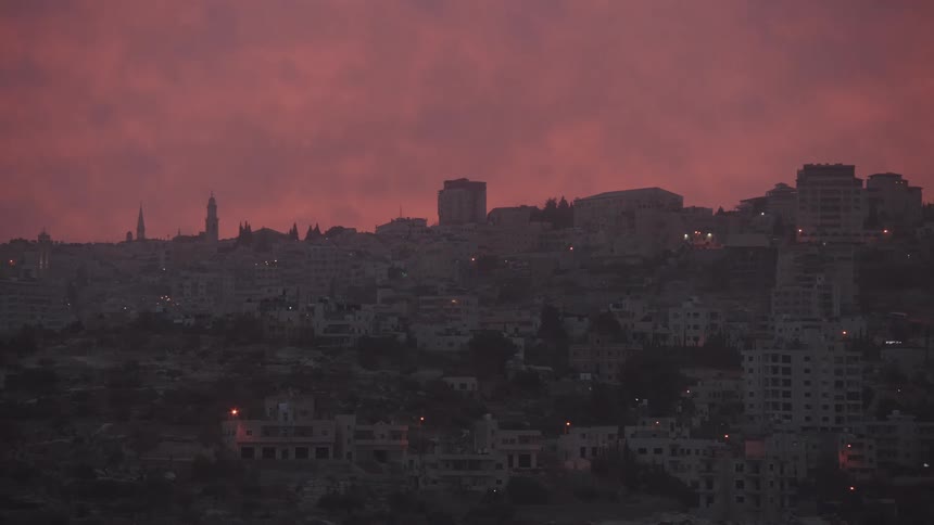 A wide, static shot of a Middle Eastern city skyline under a dramatic, fiery pink sky at dusk