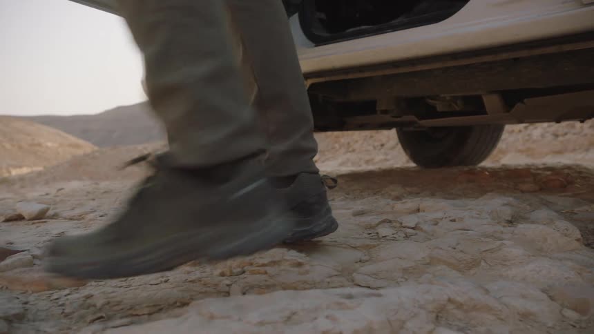 A close-up slow-motion shot of a man in hiking boots getting out of a pickup truck and walking in a rocky desert