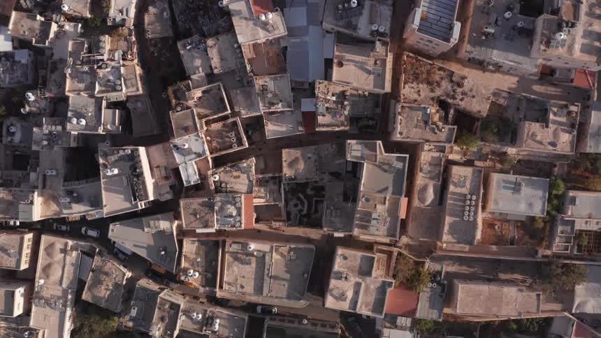 A slow top-down aerial ascent reveals the labyrinthine streets and ancient rooftops of an old city at sunrise