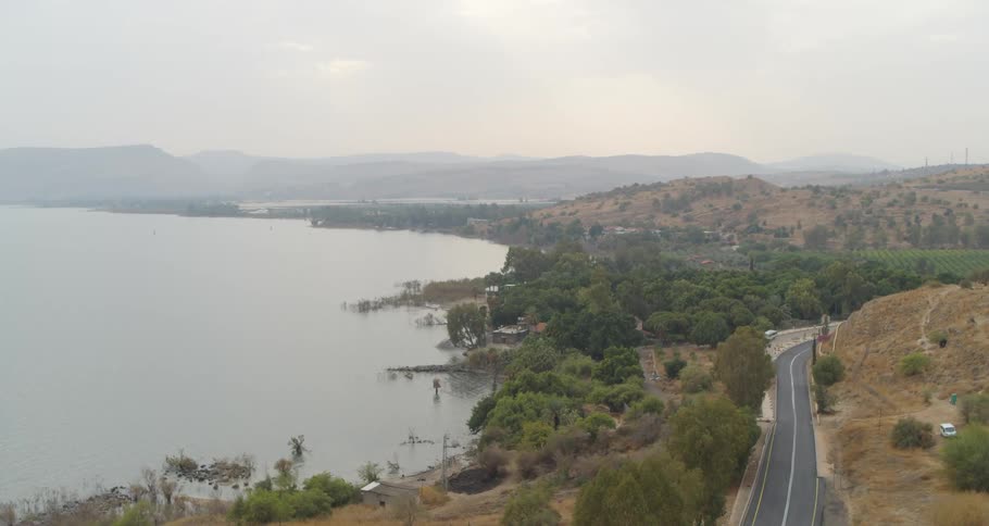 Aerial view of the Sea of Galilee coastline, with a road winding through the hilly landscape on a hazy day
