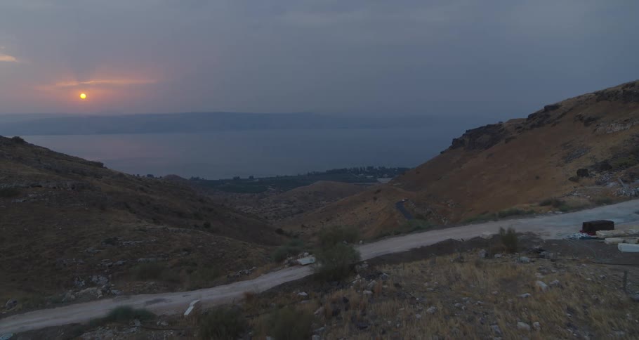 An aerial view slowly advances over a rugged valley leading to the Sea of Galilee at sunrise