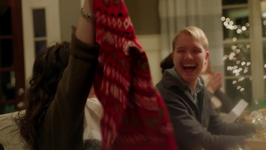 Woman opens present at table with group of people to reveal ugly christmas sweater