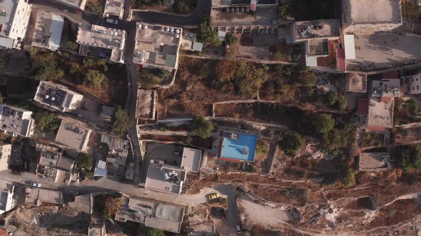 Slowly rising top-down drone shot reveals a bright blue swimming pool nestled amongst the ancient buildings of a hillside city