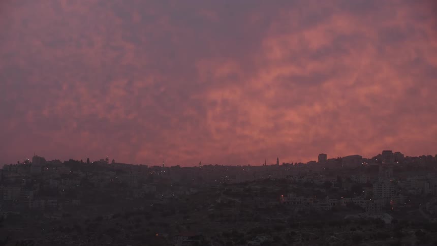 A dramatic pink and purple sunset illuminates the clouds over a city skyline at dusk