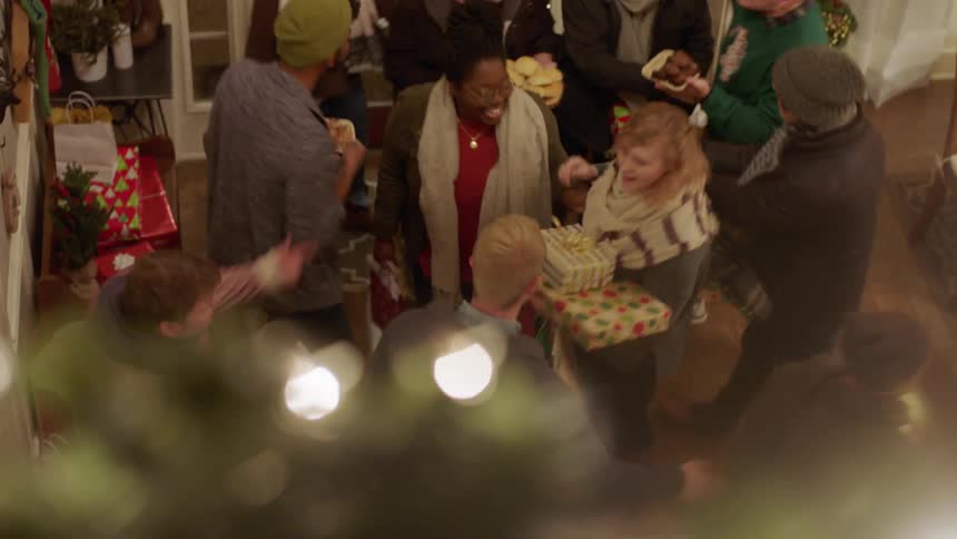 A group of people with christmas gifts greet each other in the foyer of a house