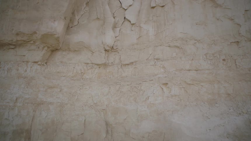 A slow, low-angle upward tilt reveals the rough, textured surface of a massive white chalk cliff