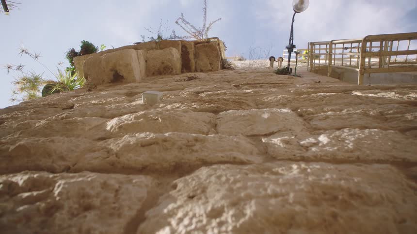 A ground-level tracking shot reveals the detailed texture of an ancient stone wall under a bright sky