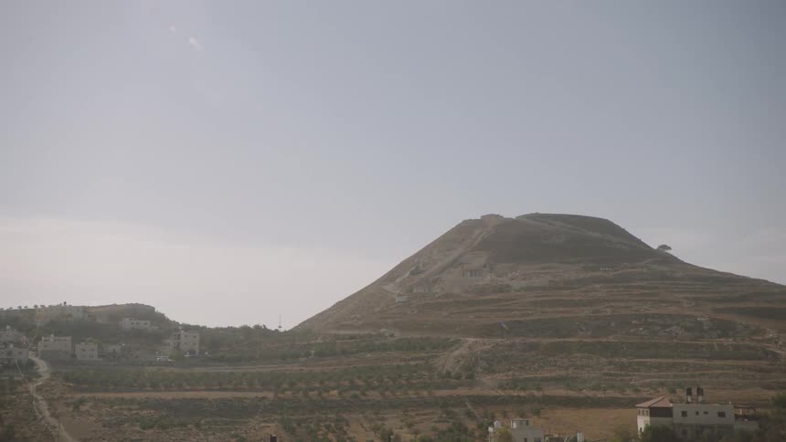A wide, static shot of the ancient Herodium fortress hill in the hazy Judean desert