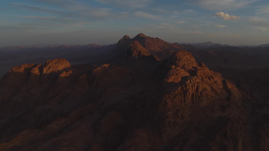 A static aerial view shows the majestic, rocky mountain peaks of Mount Sinai illuminated by the warm light of sunrise