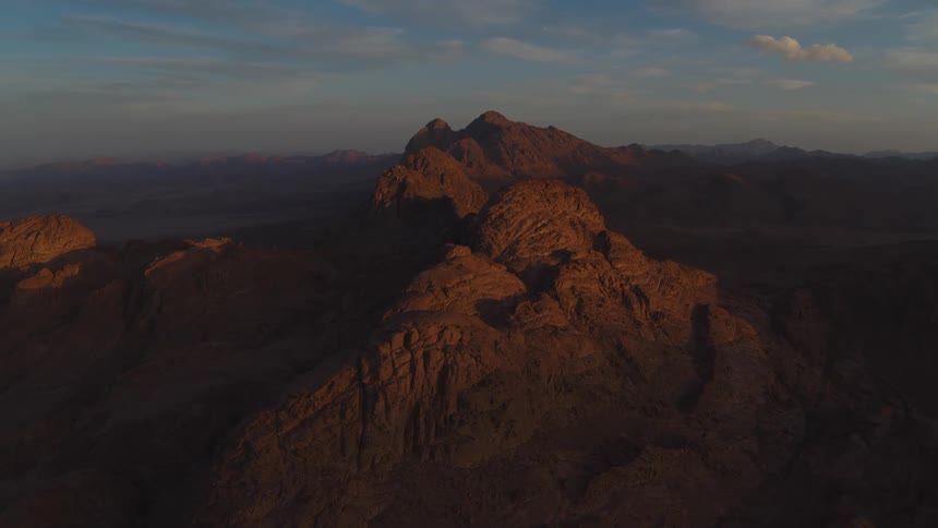 A static aerial view of the majestic Mount Sinai in Egypt as the sun rises, casting a warm golden glow on the rocky peaks
