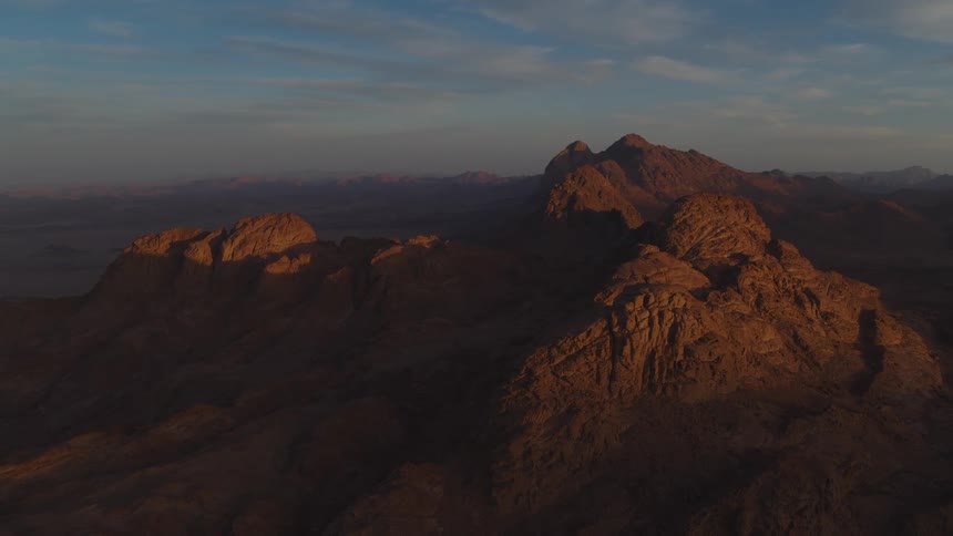 A serene, static view of a vast desert mountain range illuminated by the warm light of a golden hour sunrise