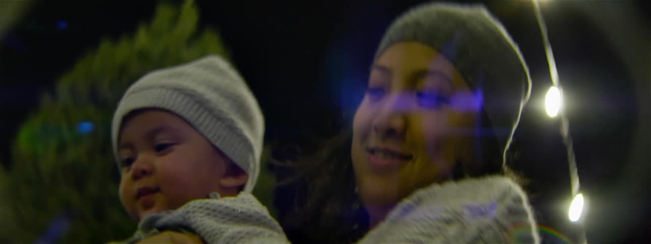 Woman holding and kissing an infant on an evening outdoors