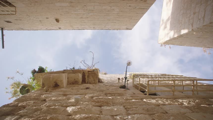 A worm's-eye view of ancient stone buildings in a narrow alley against a bright blue sky