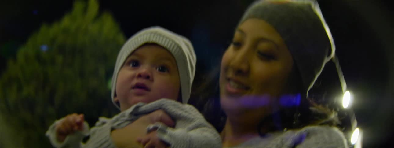 A woman kisses a baby while standing outside at night