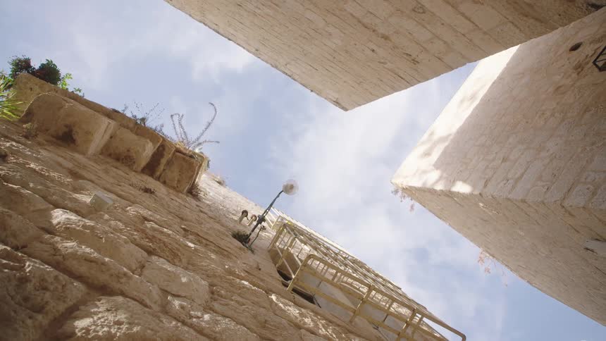 A low-angle view looking up at the bright sky from a narrow alley between ancient stone buildings