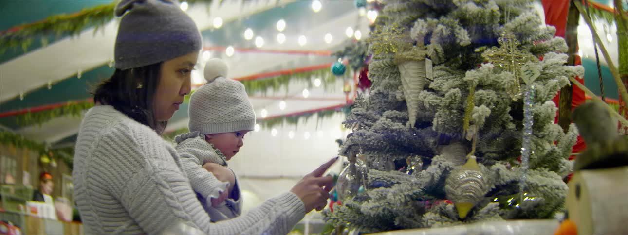 A woman holding a baby and looking at decorations on a tree