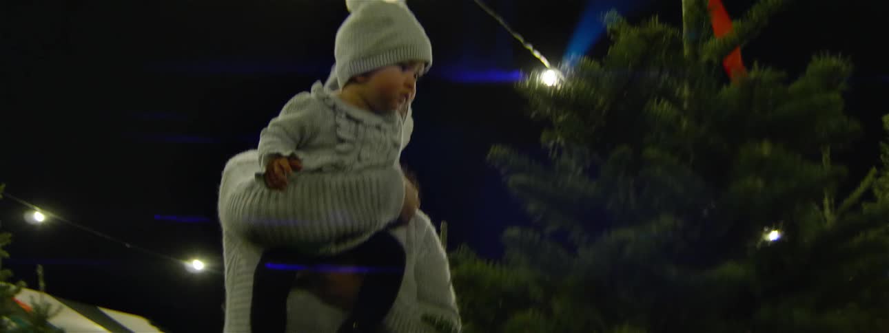 A woman holds a baby while browsing a christmas tree lot