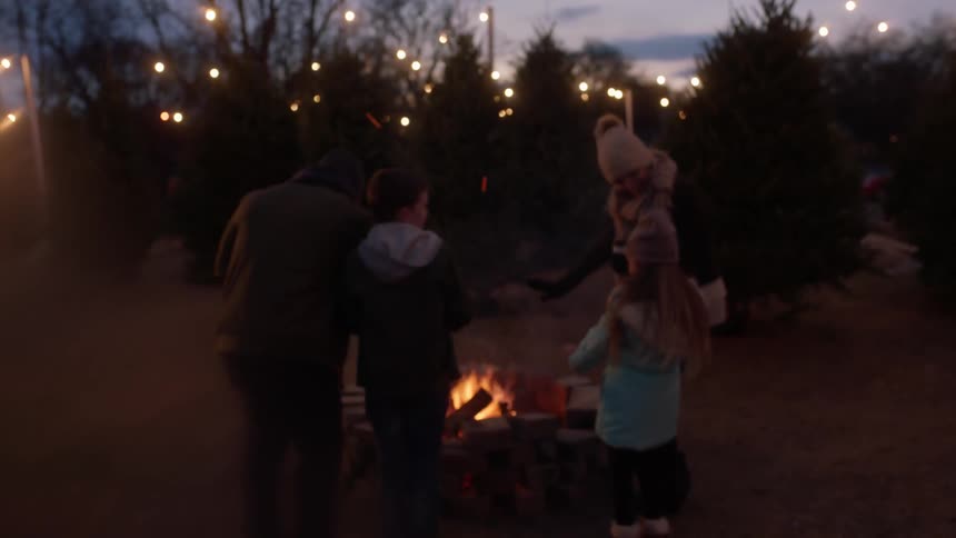 A family gathers around a bonfire at a christmas tree lot