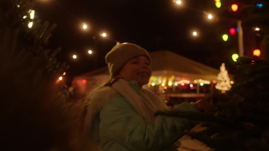 Little girl smiling while looking at christmas pine tree at night