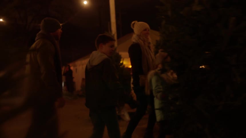 A family looks at trees in a christmas tree lot at night