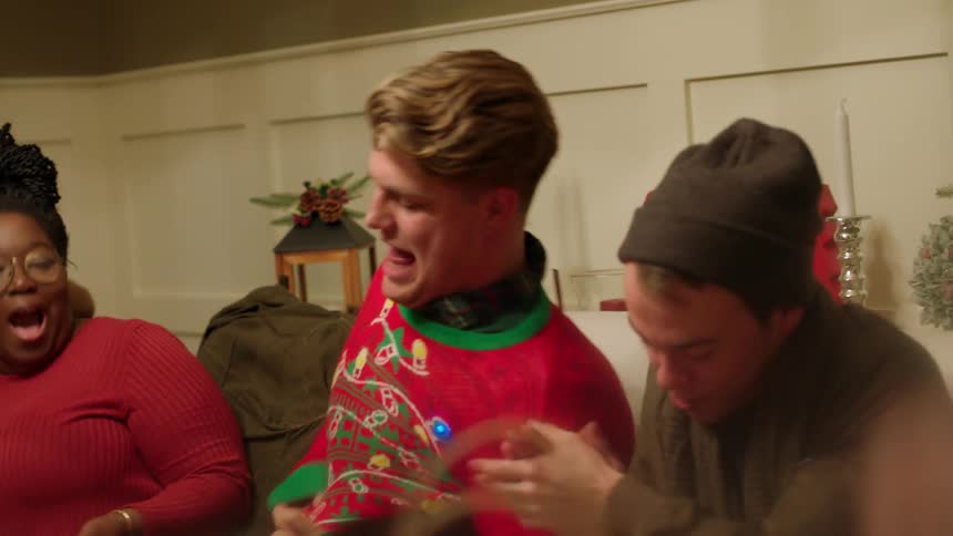 A man puts on a christmas sweater as people watch on