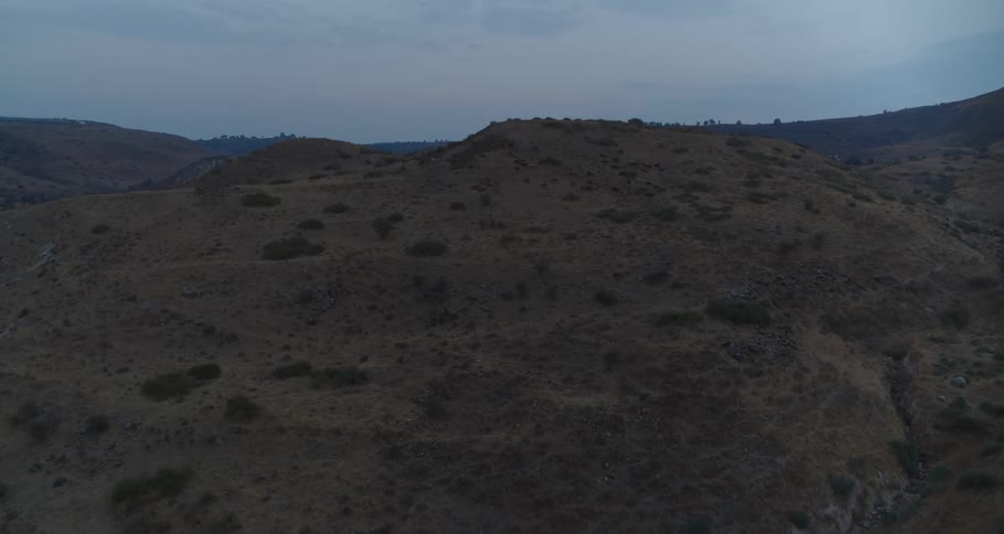 An expansive aerial view slowly pushes over a desolate, arid hillscape under a quiet twilight sky