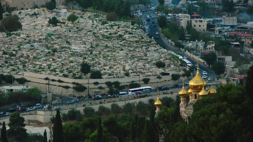 An elevated view captures the bustling traffic near the historic Mount of Olives cemetery and the golden domes of the Church of Mary Magdalene in Jerusalem