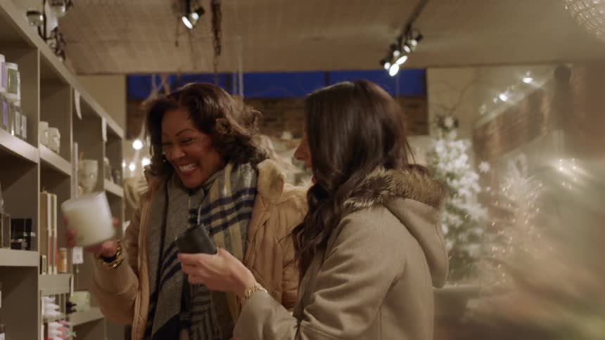 Two women talk and smell candles in a shop