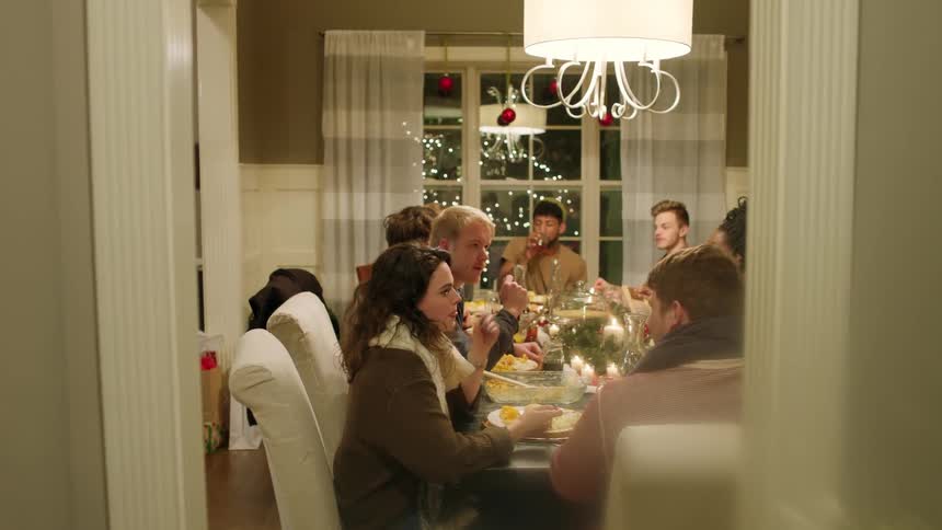 Group of people sitting at christmas dinner table talking and eating