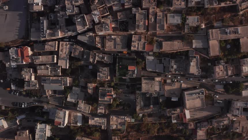 A static top-down aerial view of the rooftops and narrow streets of a historic Middle Eastern city during golden hour