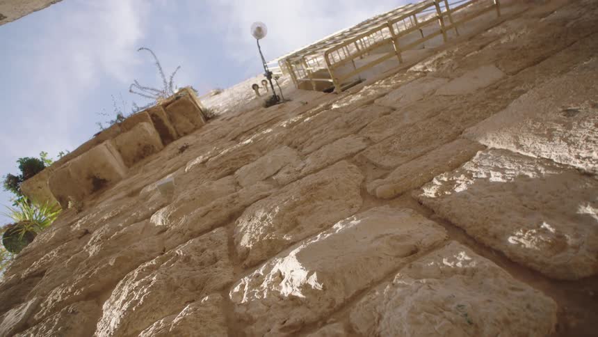 A slow, low-angle shot reveals an ancient stone wall bathed in sunlight, reaching towards the sky