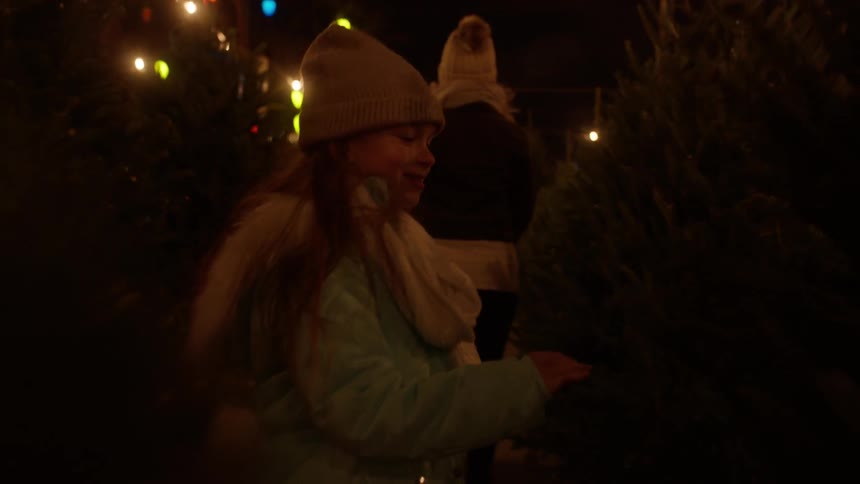 A girl looks at a tree in a christmas tree lot at night
