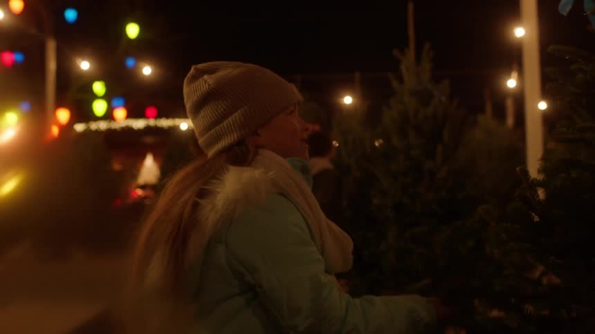 A girl looks at a tree in a christmas tree lot