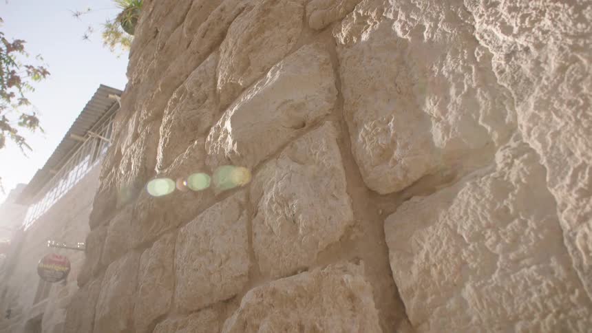A low-angle, slow-moving close-up of a sun-drenched ancient stone wall with a prominent lens flare