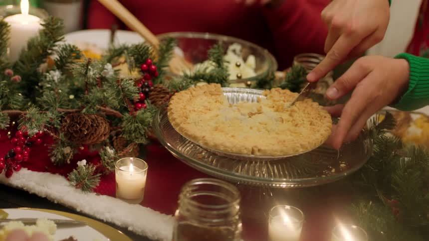 Person cuts slice of pie at christmas decorated dinner table