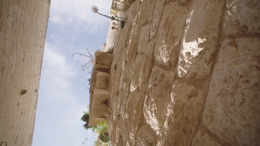 Vertical low-angle view of a sun-dappled ancient stone wall in a historic city alley