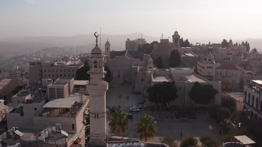 Aerial footage glides over the historic rooftops of Bethlehem, passing the Mosque of Omar minaret to reveal the revered Church of the Nativity