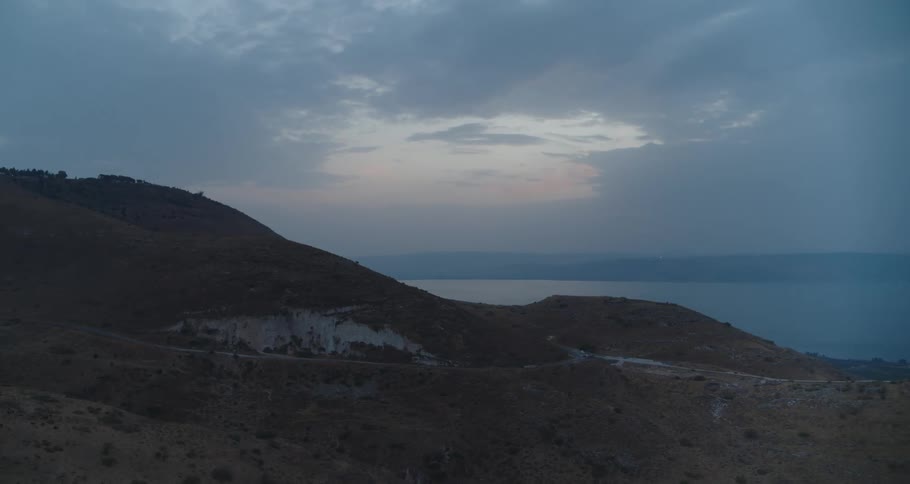 A moody twilight view of the arid hills overlooking a vast lake under a cloudy sky