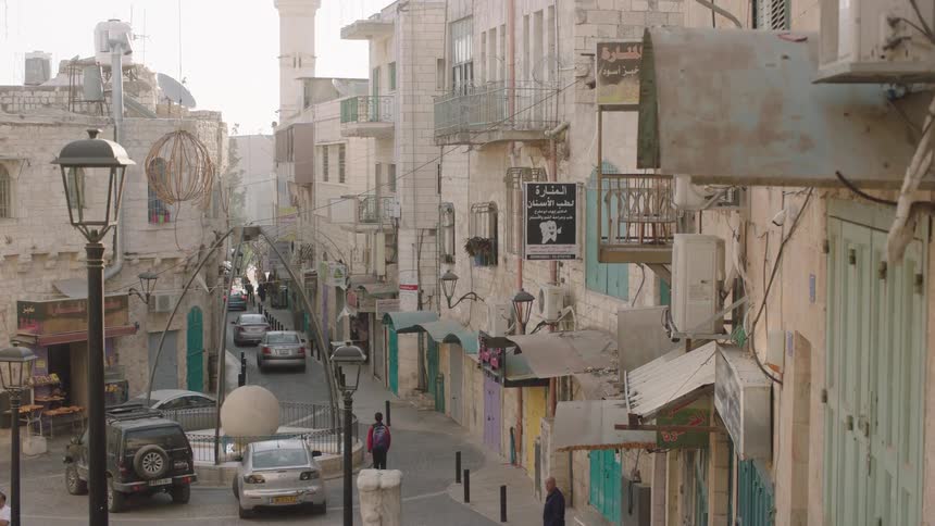 A tranquil view down a narrow, winding street in a historic Middle Eastern city with people walking by