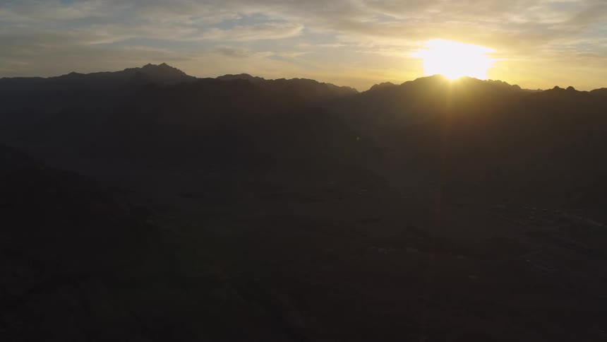An epic aerial view of the sun cresting over a silhouetted mountain range at sunrise
