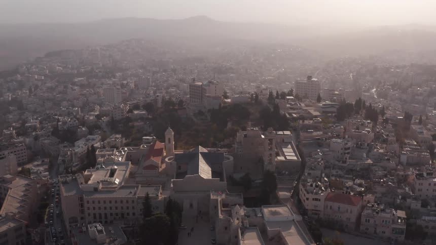 A slow, hazy aerial shot pulling back to reveal the ancient city of Bethlehem and the Church of the Nativity at sunrise