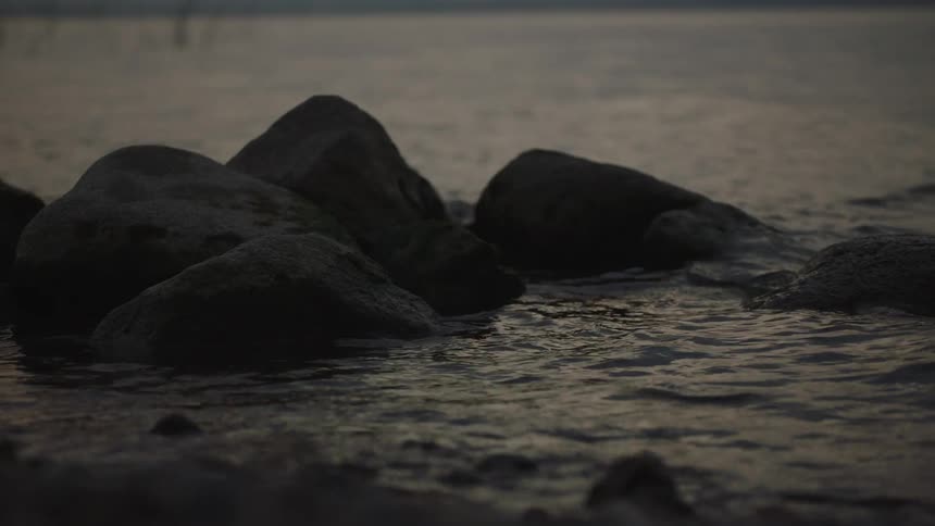 Serene view of gentle waves washing over shoreline rocks in the dim light of dusk